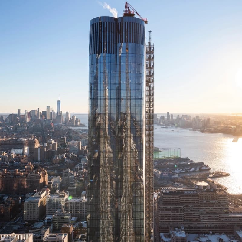 15 Hudson Yards at sunrise: a curved glass tower above the Hudson River, with Lower Manhattan behind it.