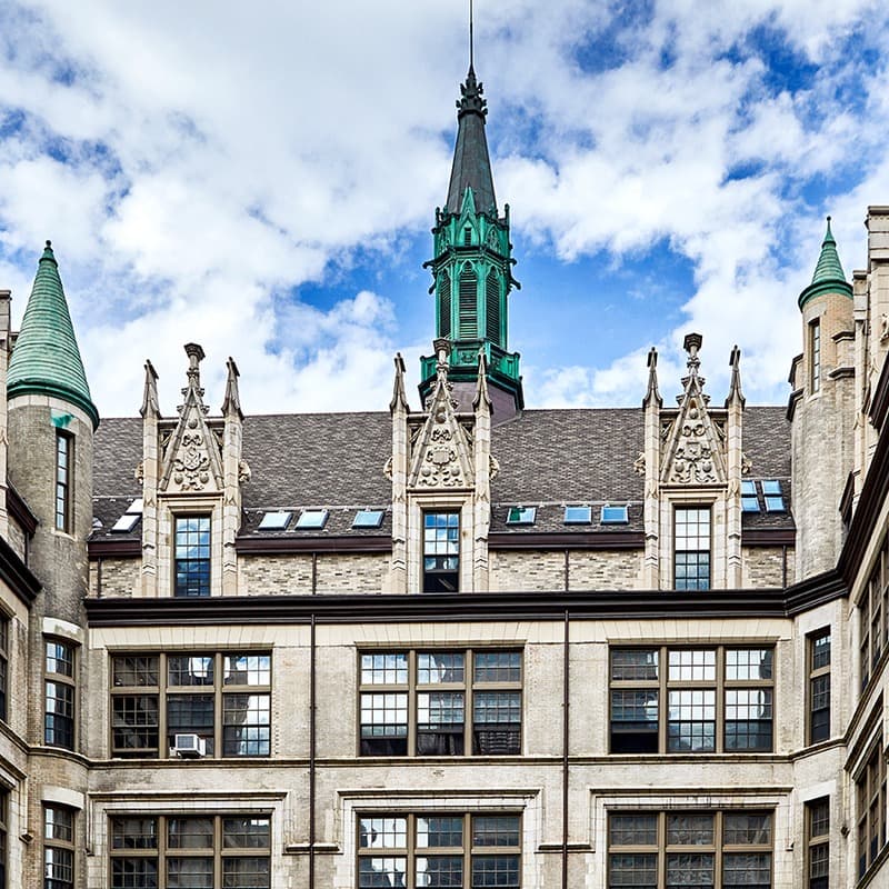 El Barrio's ArtSpace PS109 from its courtyard: a Collegiate Gothic school building in pale brick, its green copper spire against a blue sky.