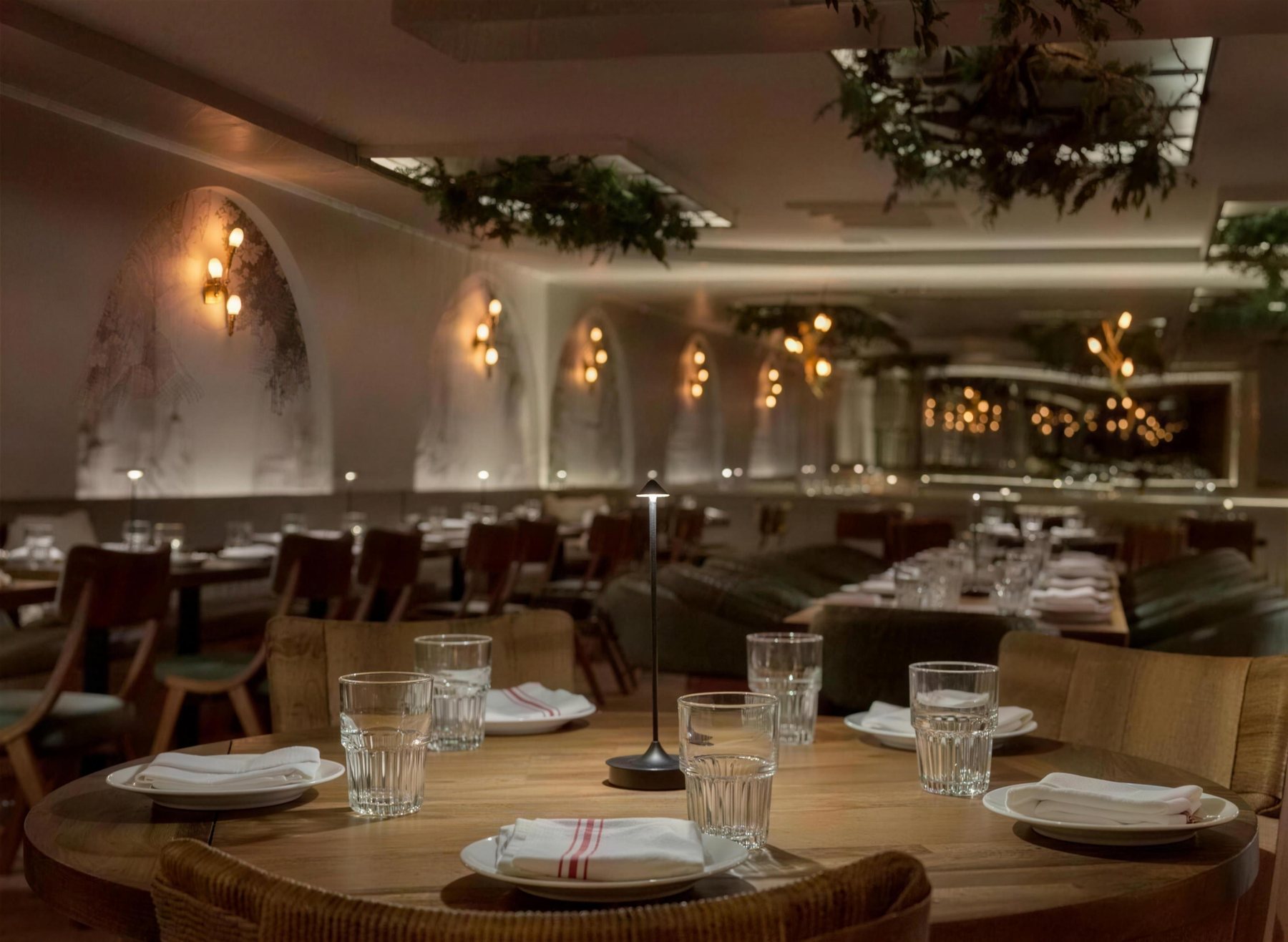 Anémi's dining room at night: arched walls, warm sconces, olive branches over the tables