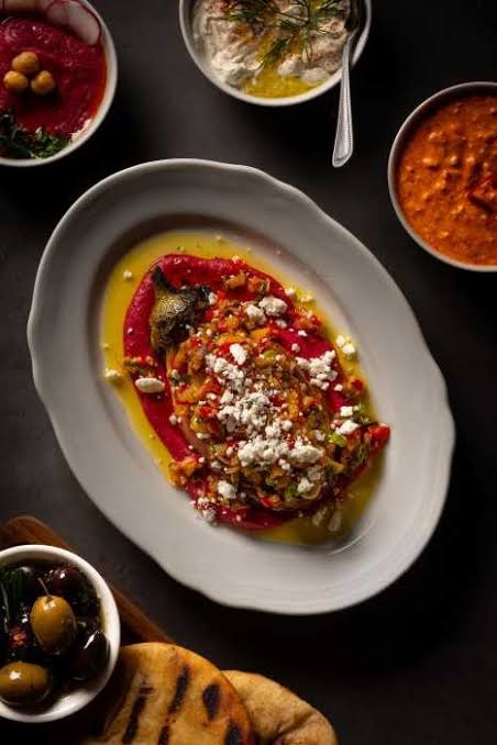 Charred eggplant with crumbled feta on a red pepper spread, olives, pita and dips around it