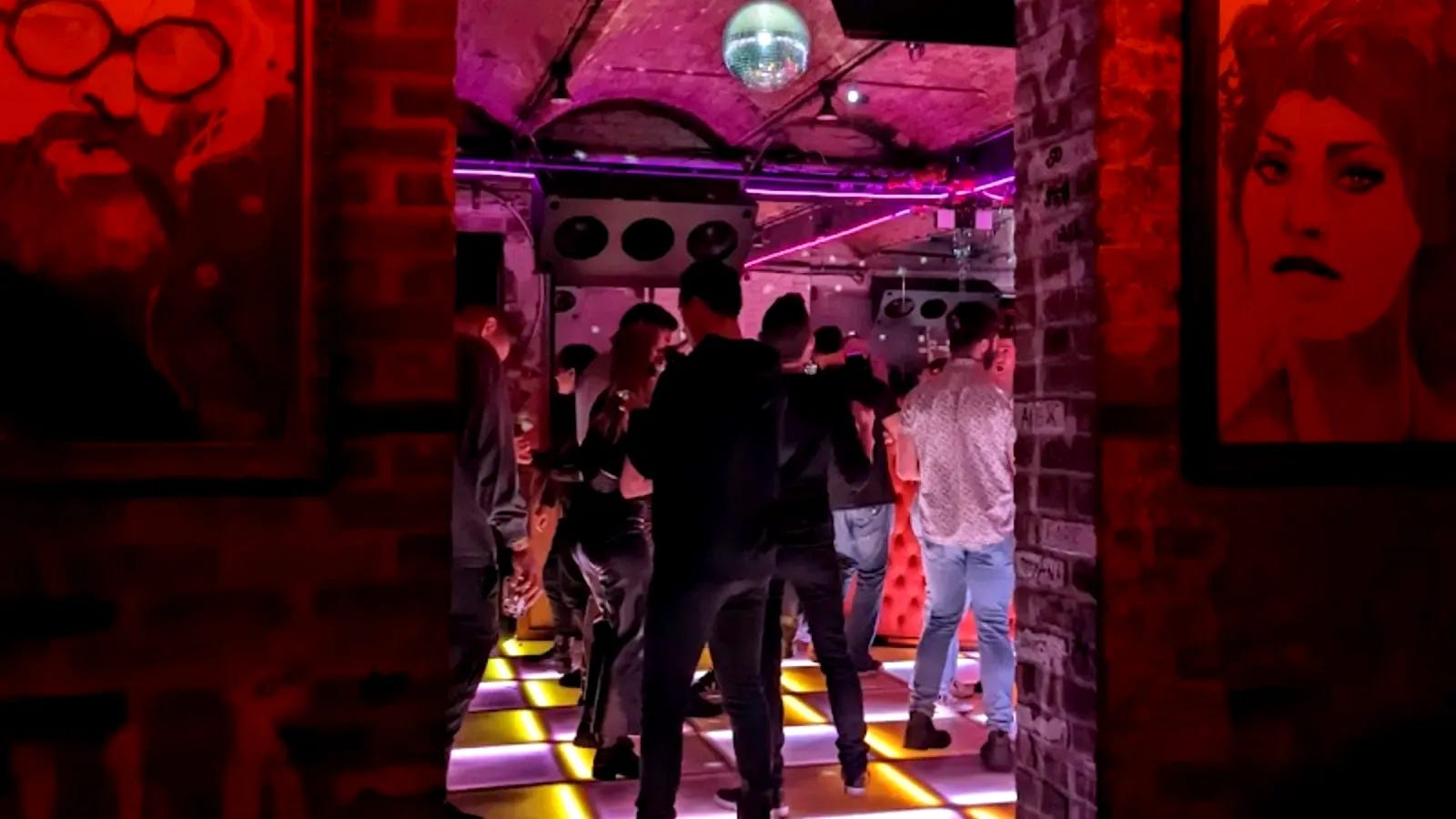 Dancers on the lit checkerboard floor at Ciao Ciao Disco, a mirror ball and neon tubing under the brick vault