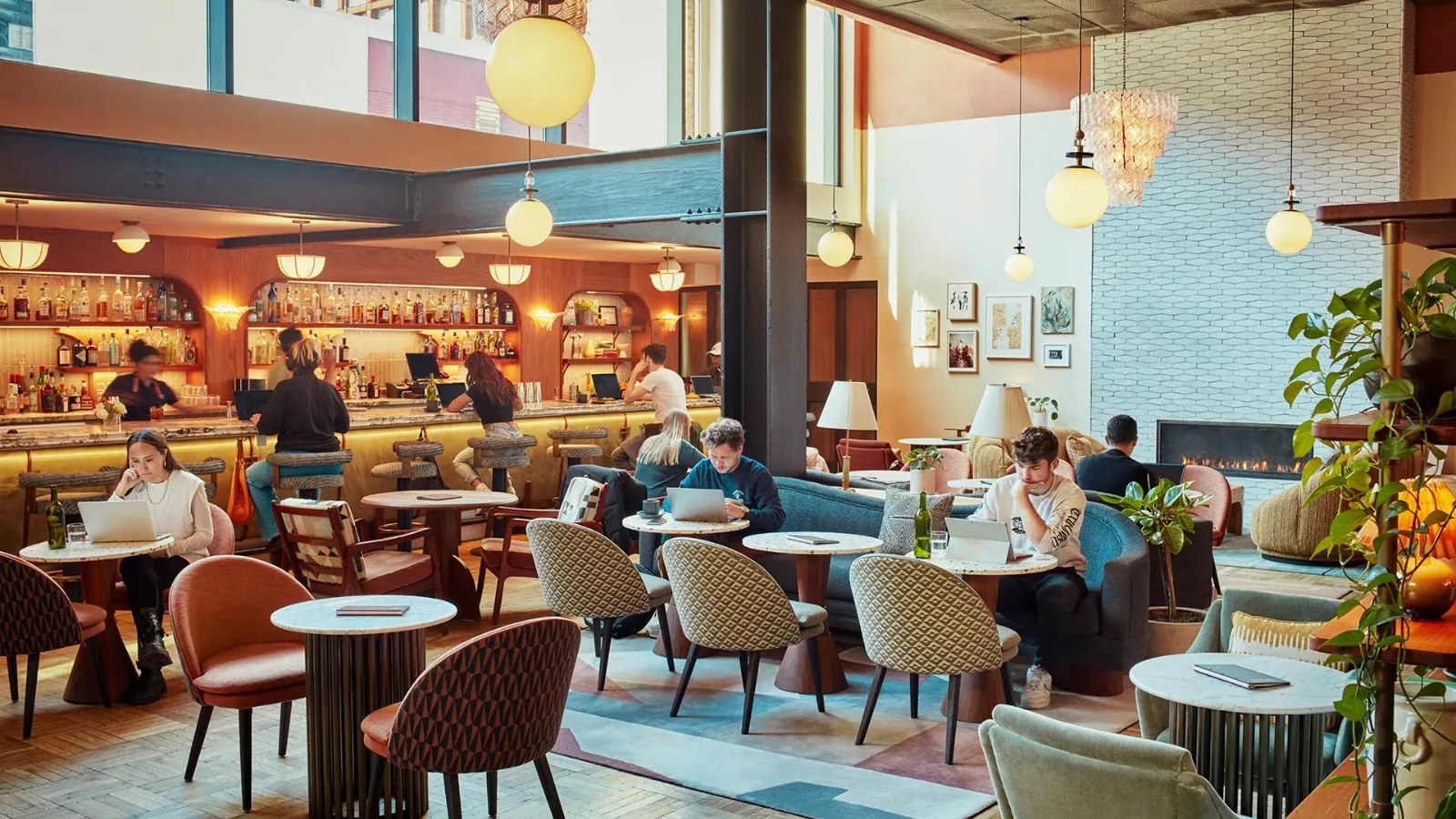 The lobby cafe at The Hoxton, Williamsburg: globe pendants over the bar, patterned armchairs, and people working at small round tables