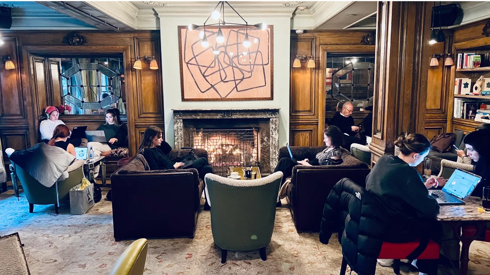 The Marlton lobby: a lit fireplace under dark panelled wood, armchairs pulled close, and people working with laptops